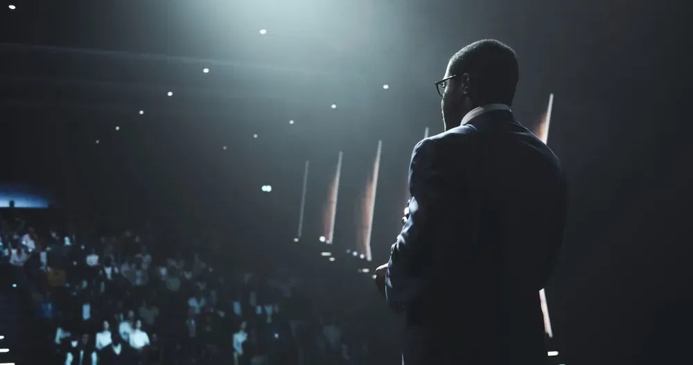 A speaker on a dark stage, facing the audience before the talk begins